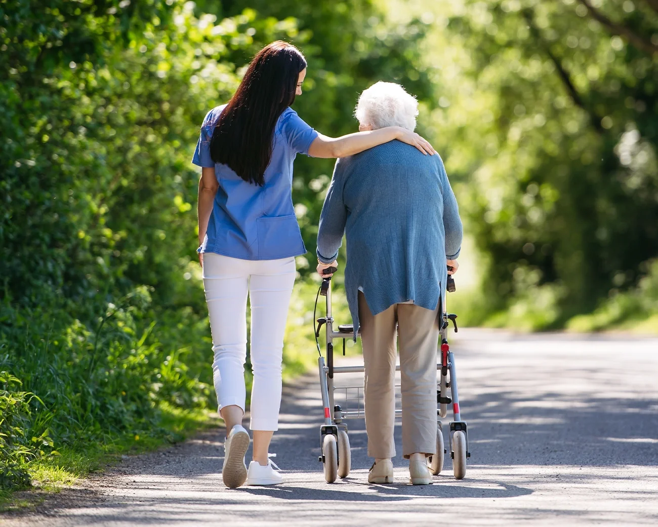 Bejaarde vrouw met rollator en begeleider