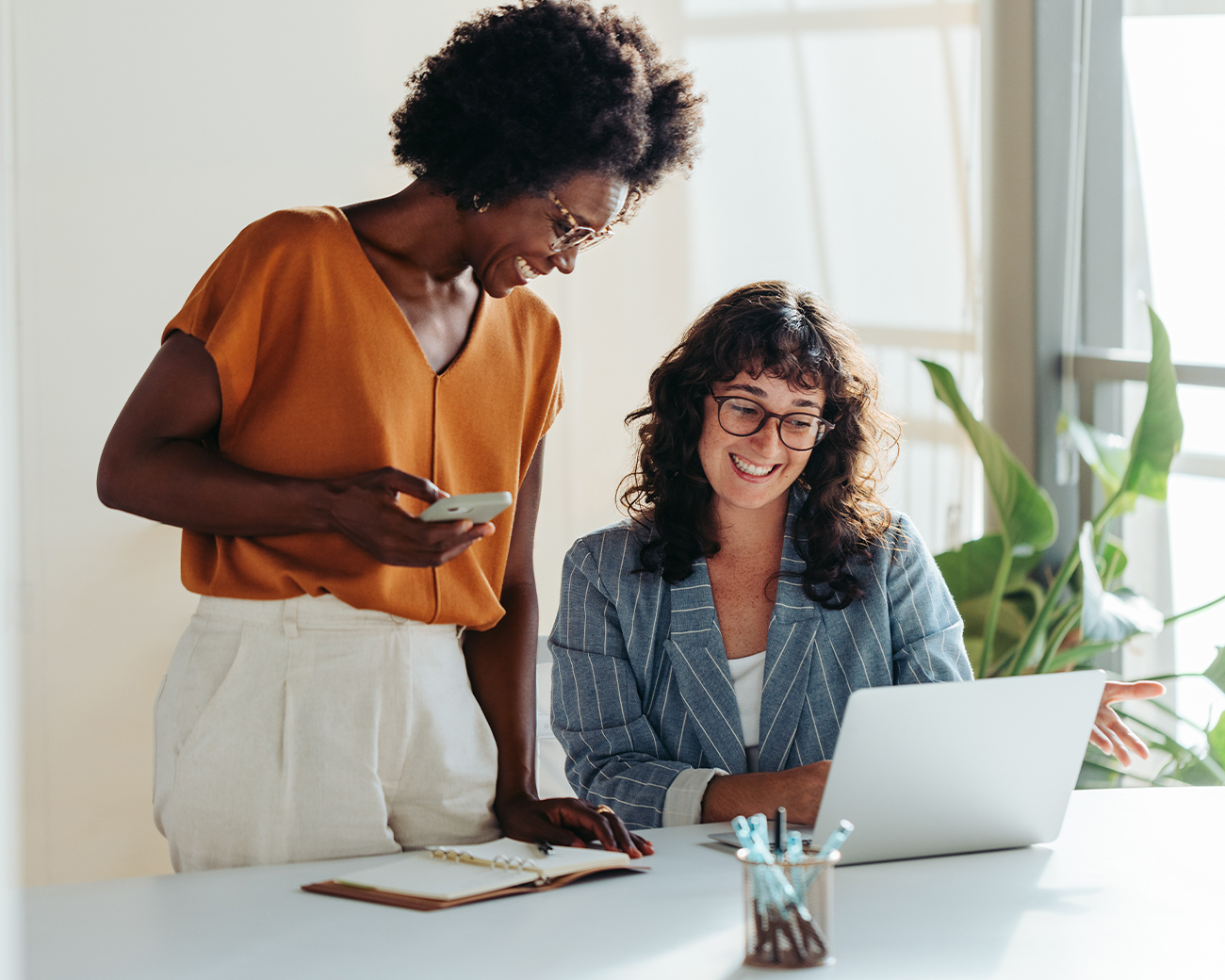 Twee vrouwen werken samen, een staat en een zit achter een laptop