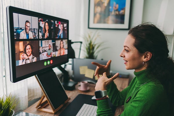 Vrouw in groene trui achter computer in videocall met collega's