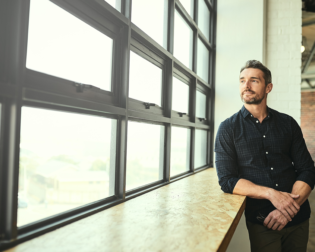 Jonge man met donker hemd kijkt uit groot raam