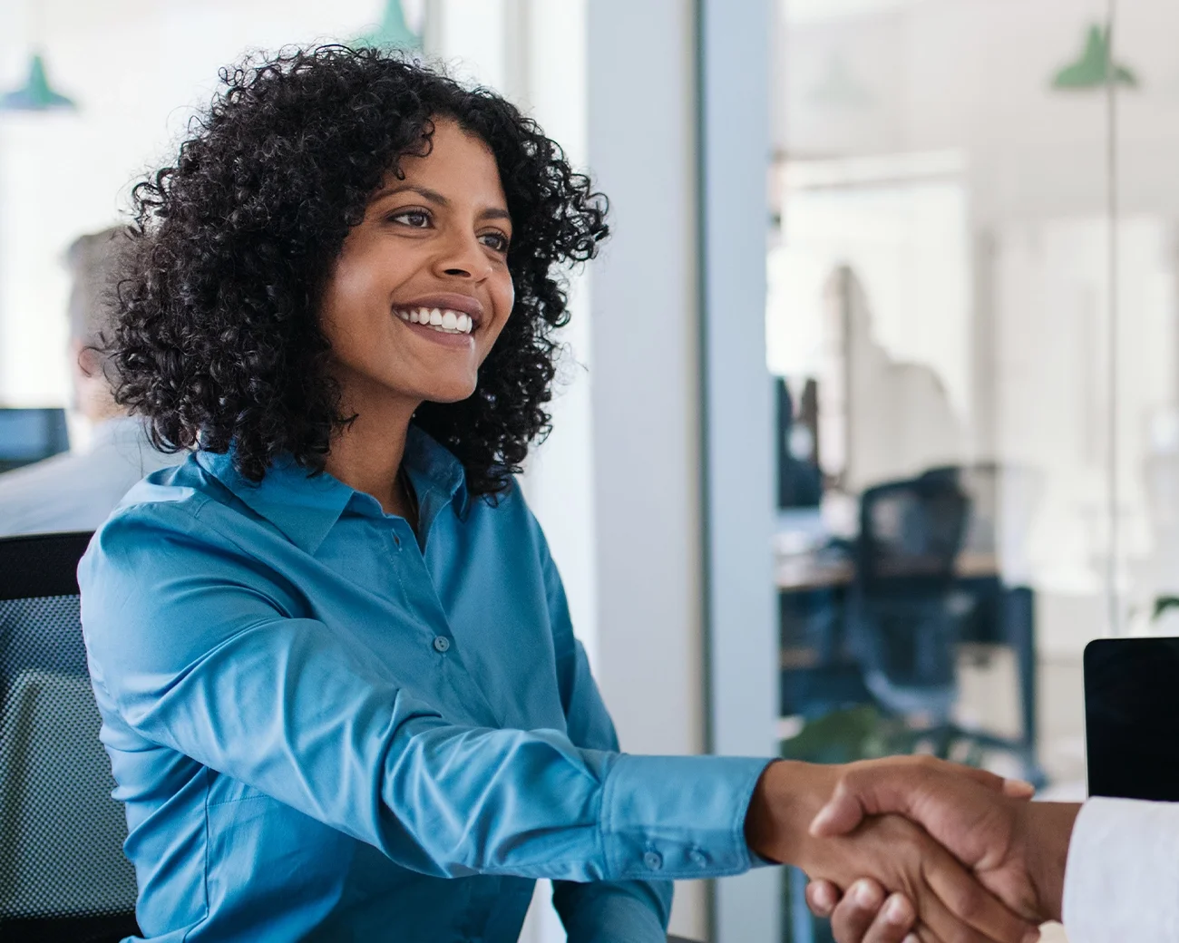 Lachende vrouw geeft persoon in kantooromgeving een hand