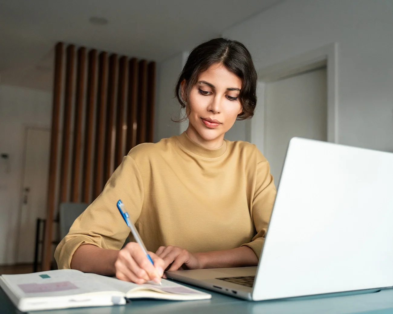 Vrouw zit achter haar laptop en schrijft mee op papier