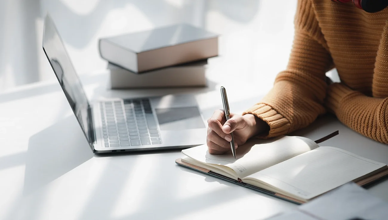 Student met laptop, schrijft iets in notebook