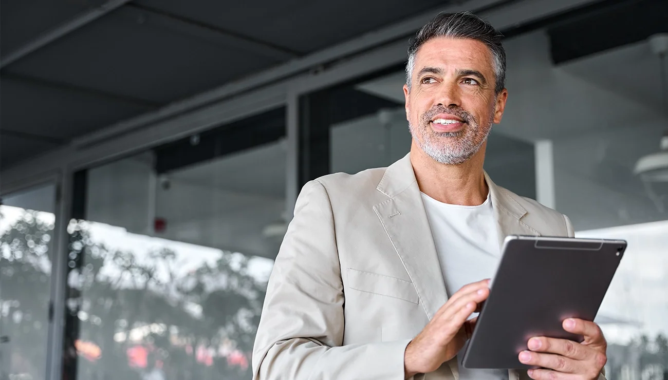 Man met beige jasje en grijze baard houdt tablet vast en kijkt opzij