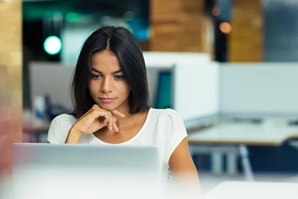 Vrouw met donker haar zit in kantoorruimte achter laptop