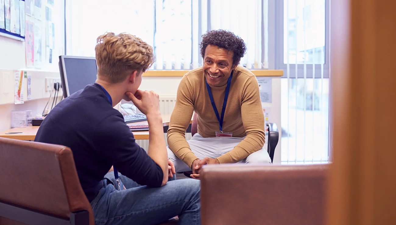 Twee personen in gesprek in een kantoor, met bureau en computer op de achtergrond
