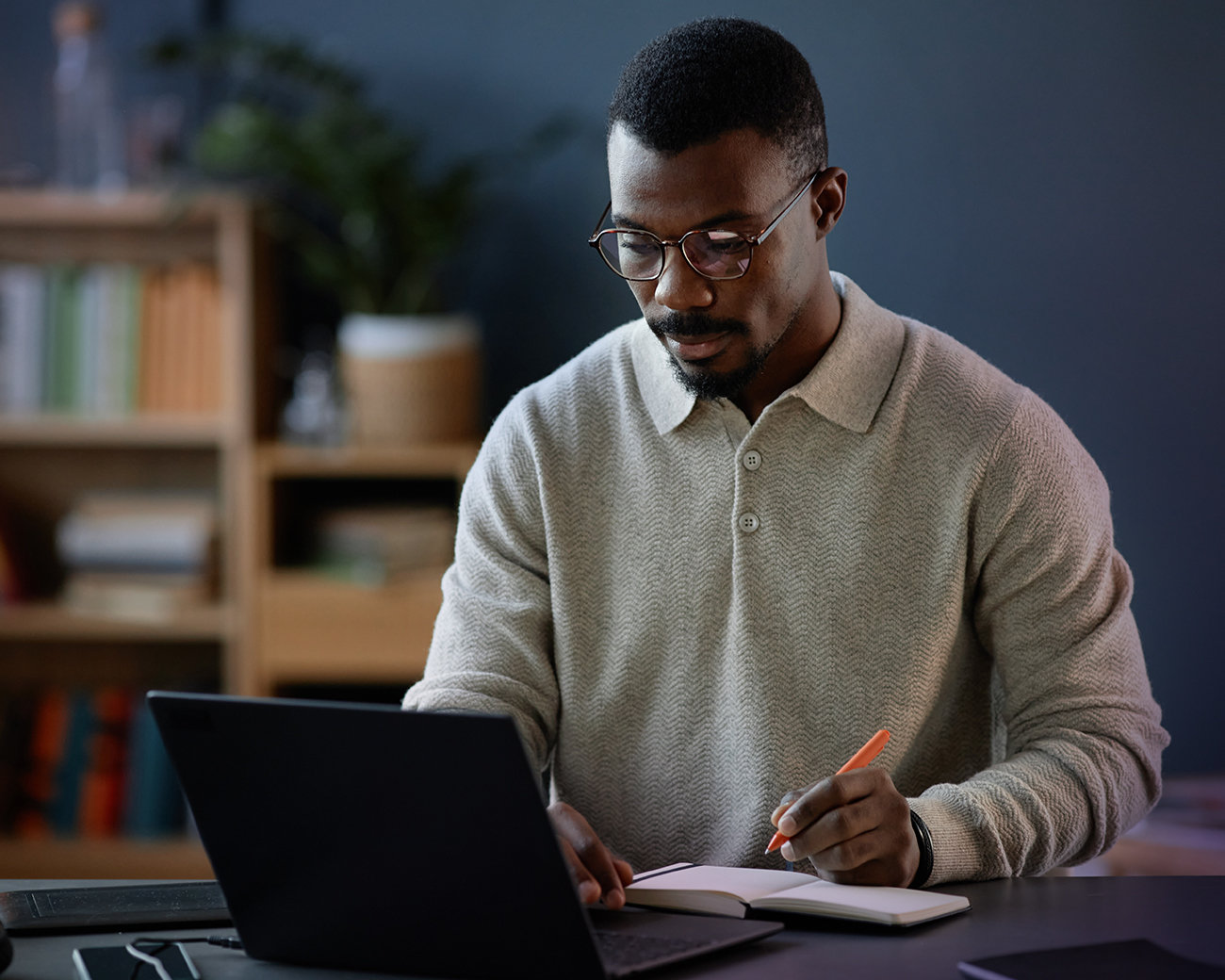 Man kijkt naar laptop en schrijft iets in notitieboek