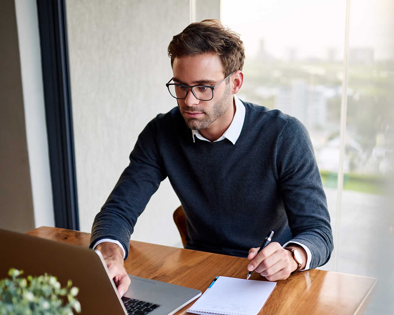 Man kijkt gefocust naar laptop en maakt aantekeningen