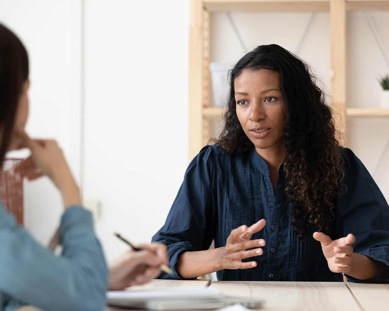 Vrouw geeft uitleg aan persoon vanachter bureau