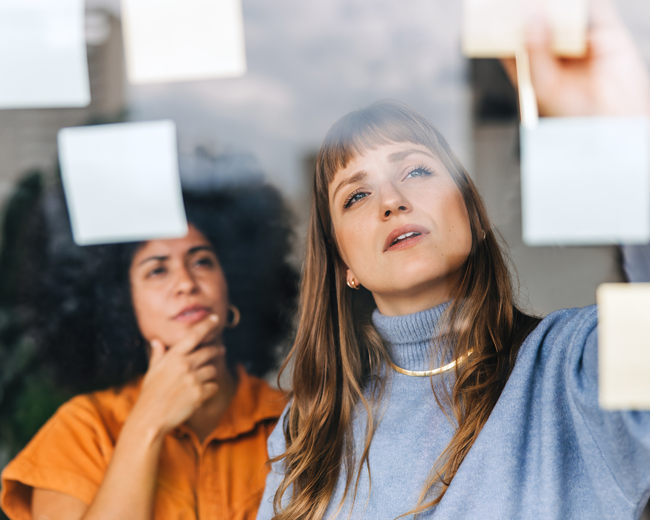 Twee vrouwen plakken sticky notes op een raam en kijken nadenkend