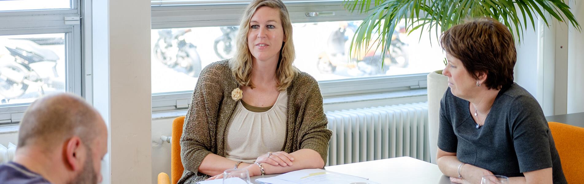 Drie mensen aan tafel in onderwijssetting