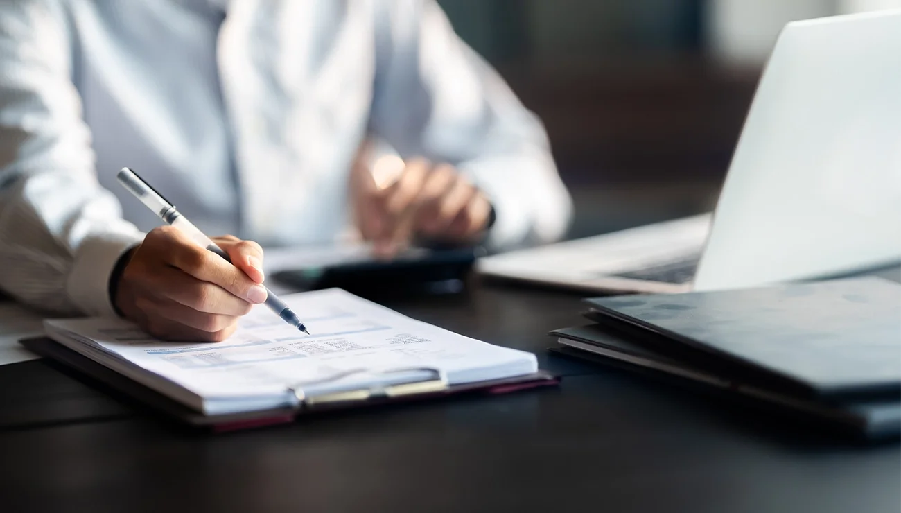 Persoon maakt notities op papier vanaf laptop