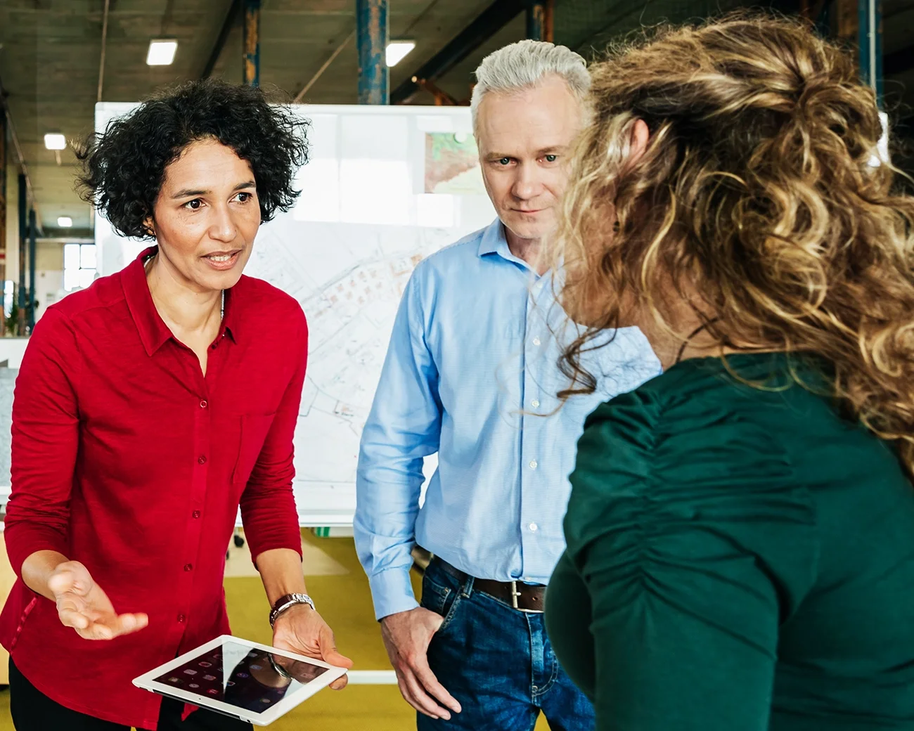 Vrouw met rode blouse en Ipad samen met twee collega's.