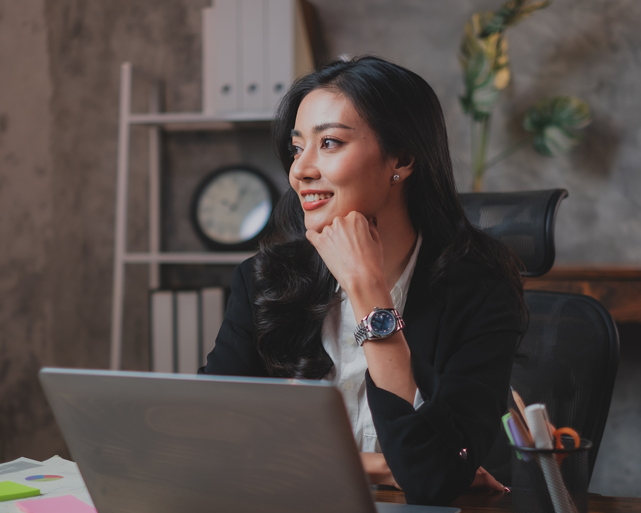 Vrouw met lang zwart haar achter laptop kijkt glimlachend opzij