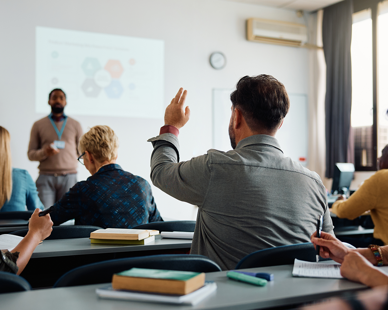 Klaslokaal van de achterkant met man in grijs hemd die zijn hand opsteekt