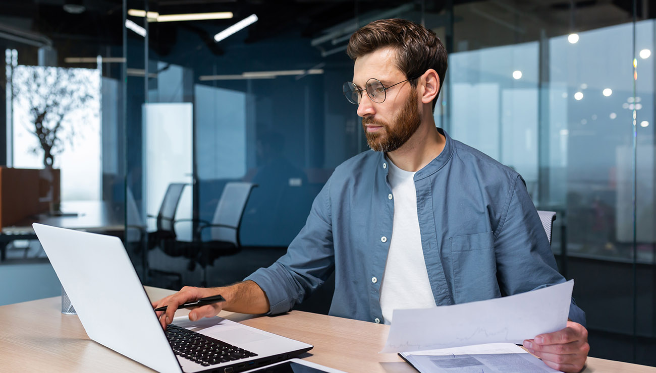 Man met baard met laptop en papier in de handen