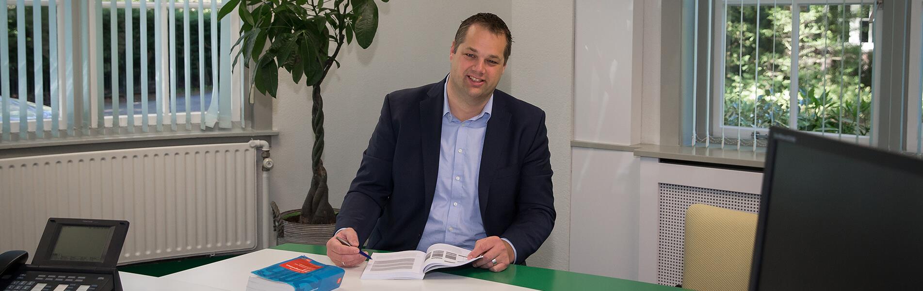 Ed van der Scheer achter een bureau met boek open op tafel