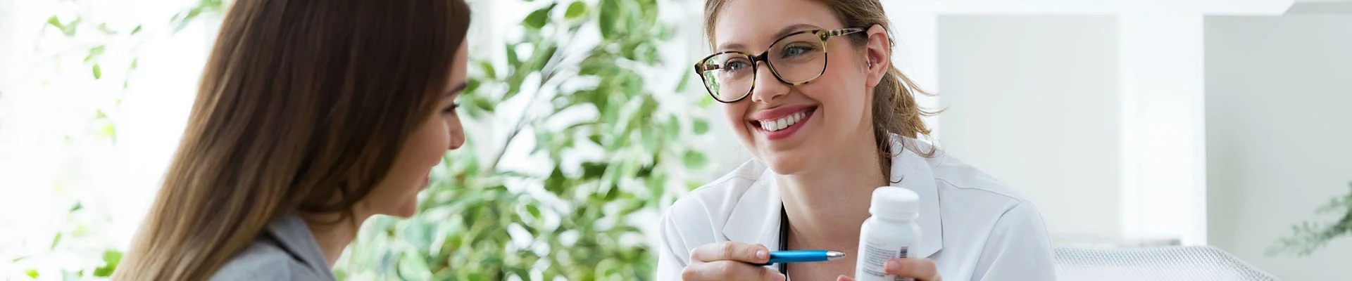 Zorgprofessional in witte blouse zit tegenover cliënt en lacht