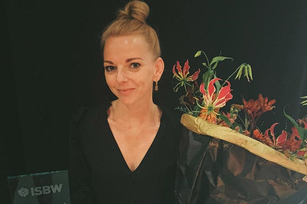 Miru Schuurman in zwarte blouse voor een achtergrond met roodgroene bloemen