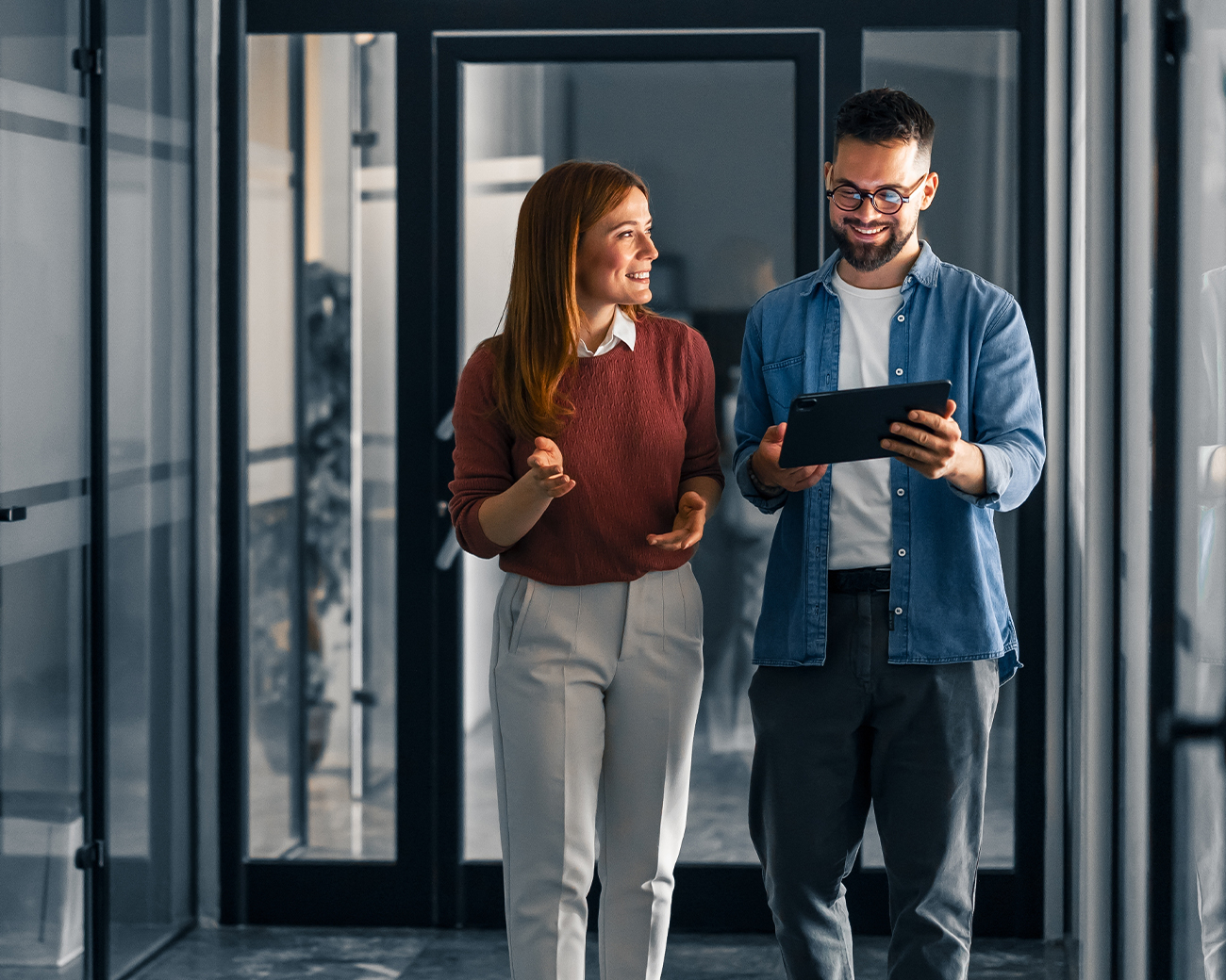 Man en vrouw in glazen kantoorsetting kijken lachend naar tablet