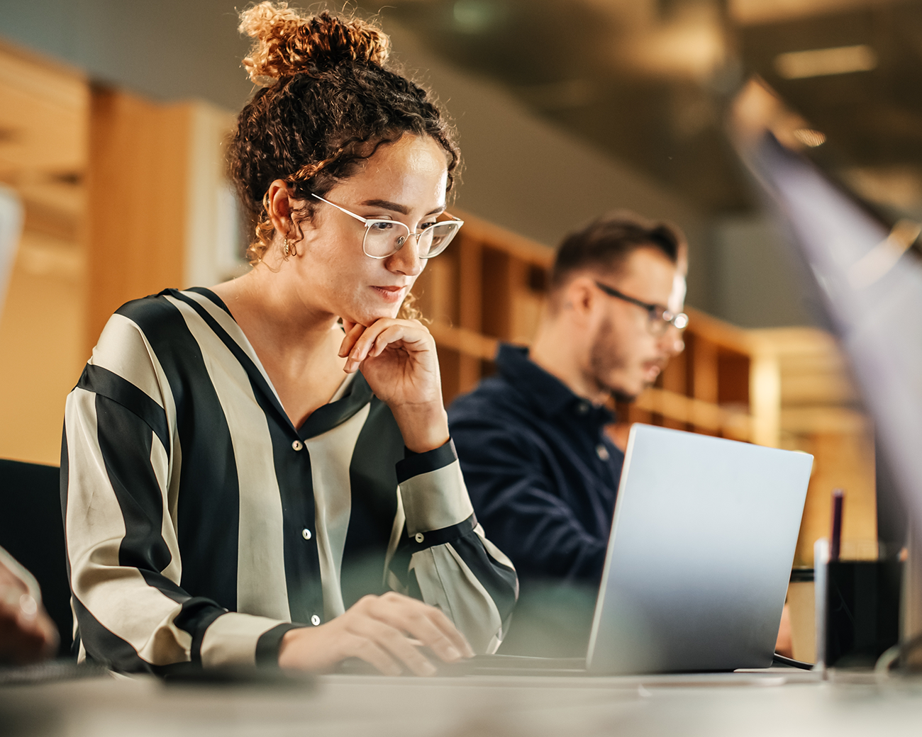 Vrouw werkt op laptop met een man op de achtergrond