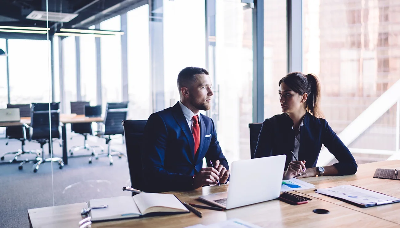 Man en vrouw in pak bespreken samen een financieel rapport aan een bureau