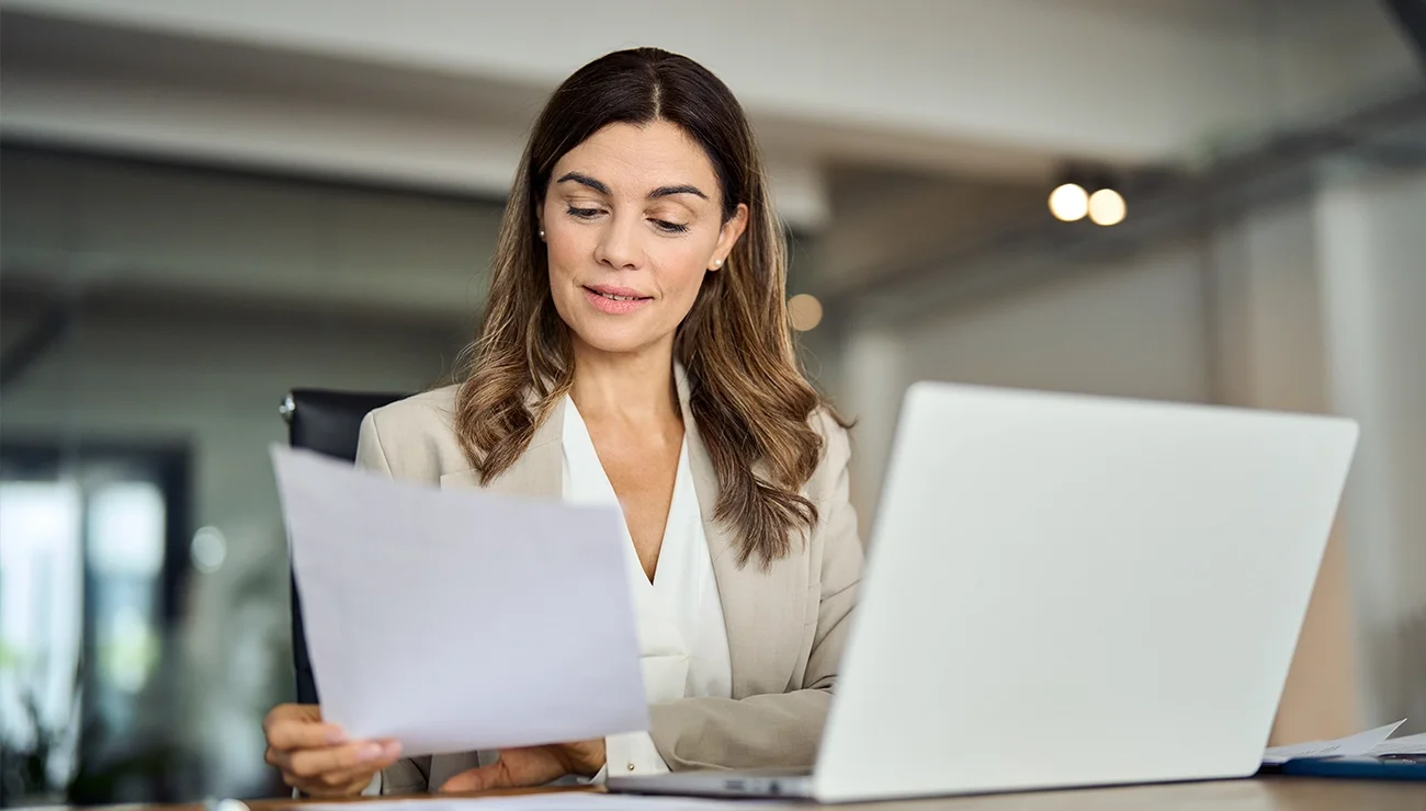 Vrouw achter laptop met A4tje in handen