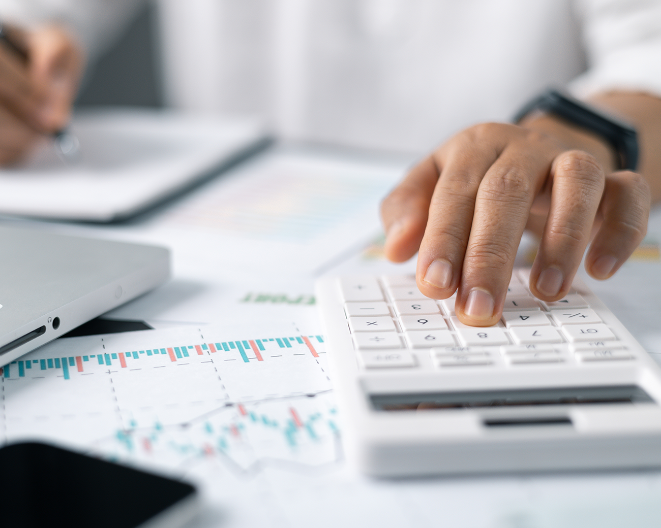 close-up van hand die iets intoetst op een rekenmachine met papieren en grafieken op het bureau
