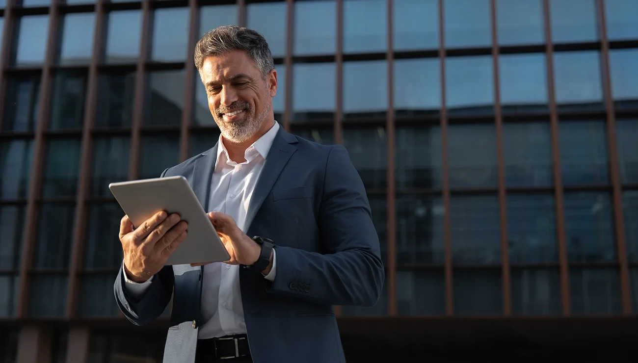 Persoon met een tablet in de hand staat voor een bedrijfspand