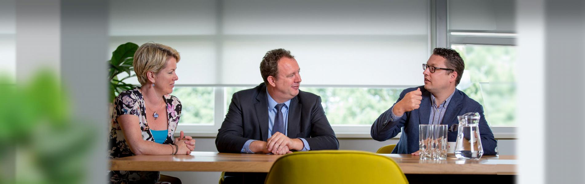 Vrouw en twee mannen in gesprek aan een vergadertafel