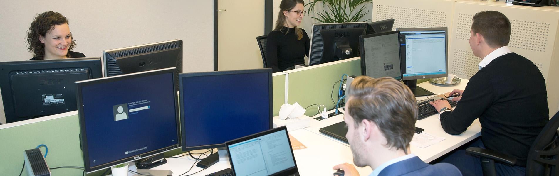 Kantoorsetting met meerdere laptop- en computerschermen en vier medewerkers