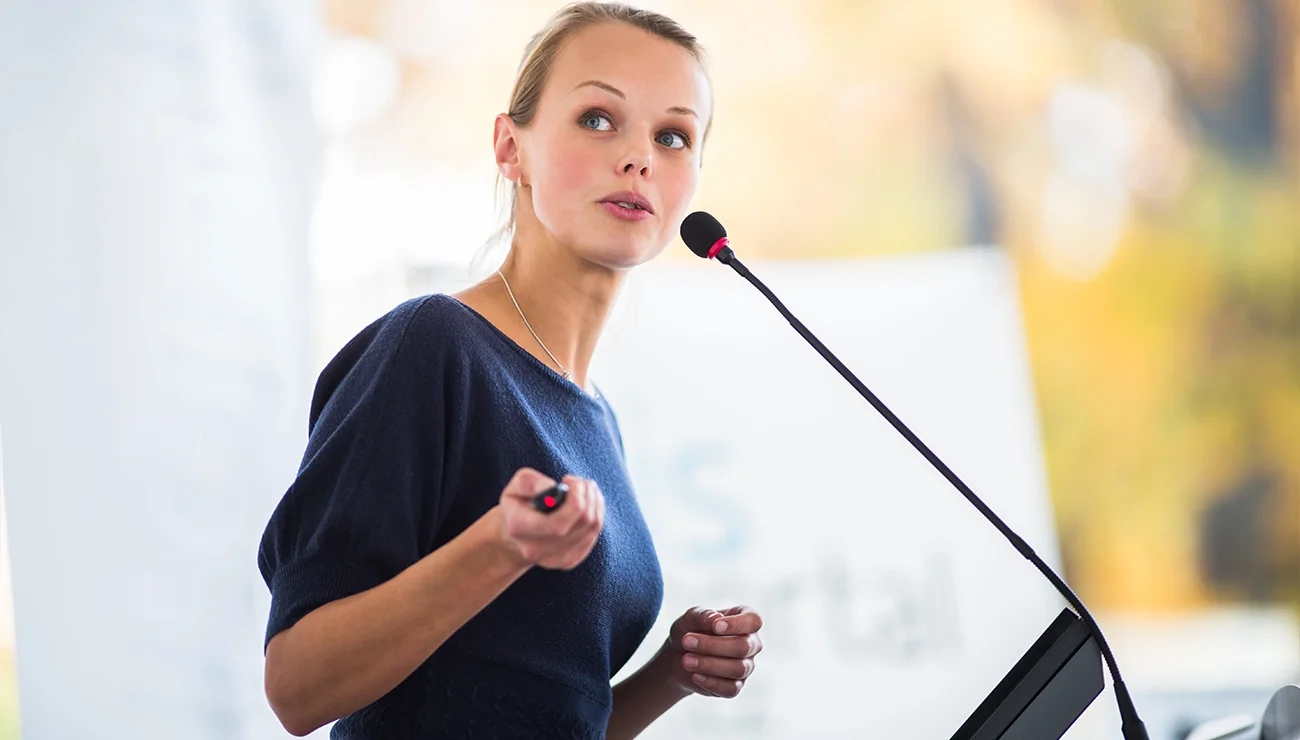 Jonge vrouw spreekt in microfoon en wijst met pointer