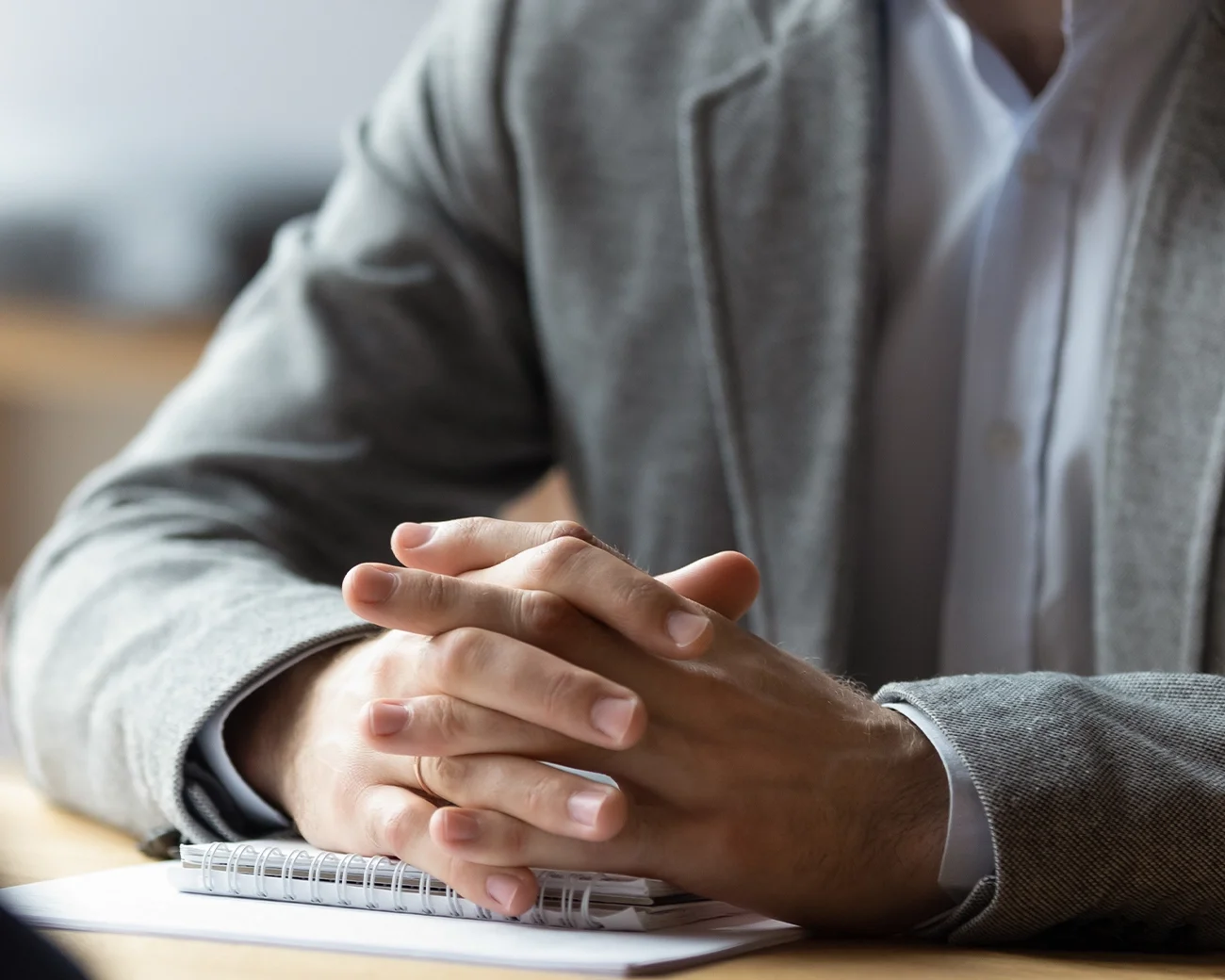 Man in pak, handen verstrengeld aan bureau.