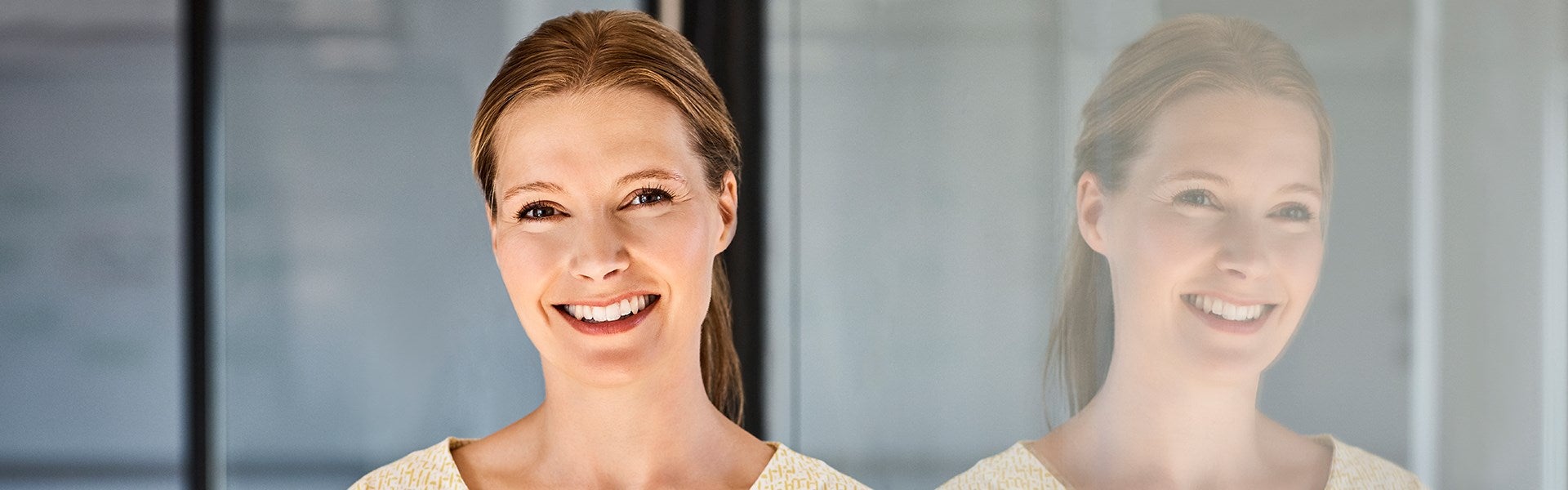 Vrouw kijkt in camera met reflectie in glazen wand