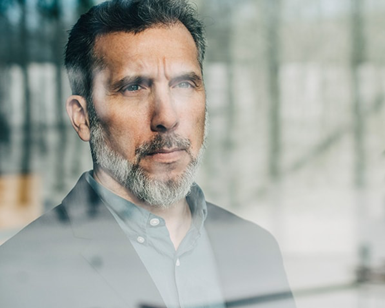 Man met grijzend haar en grijze baard kijkt peinzend uit het raam