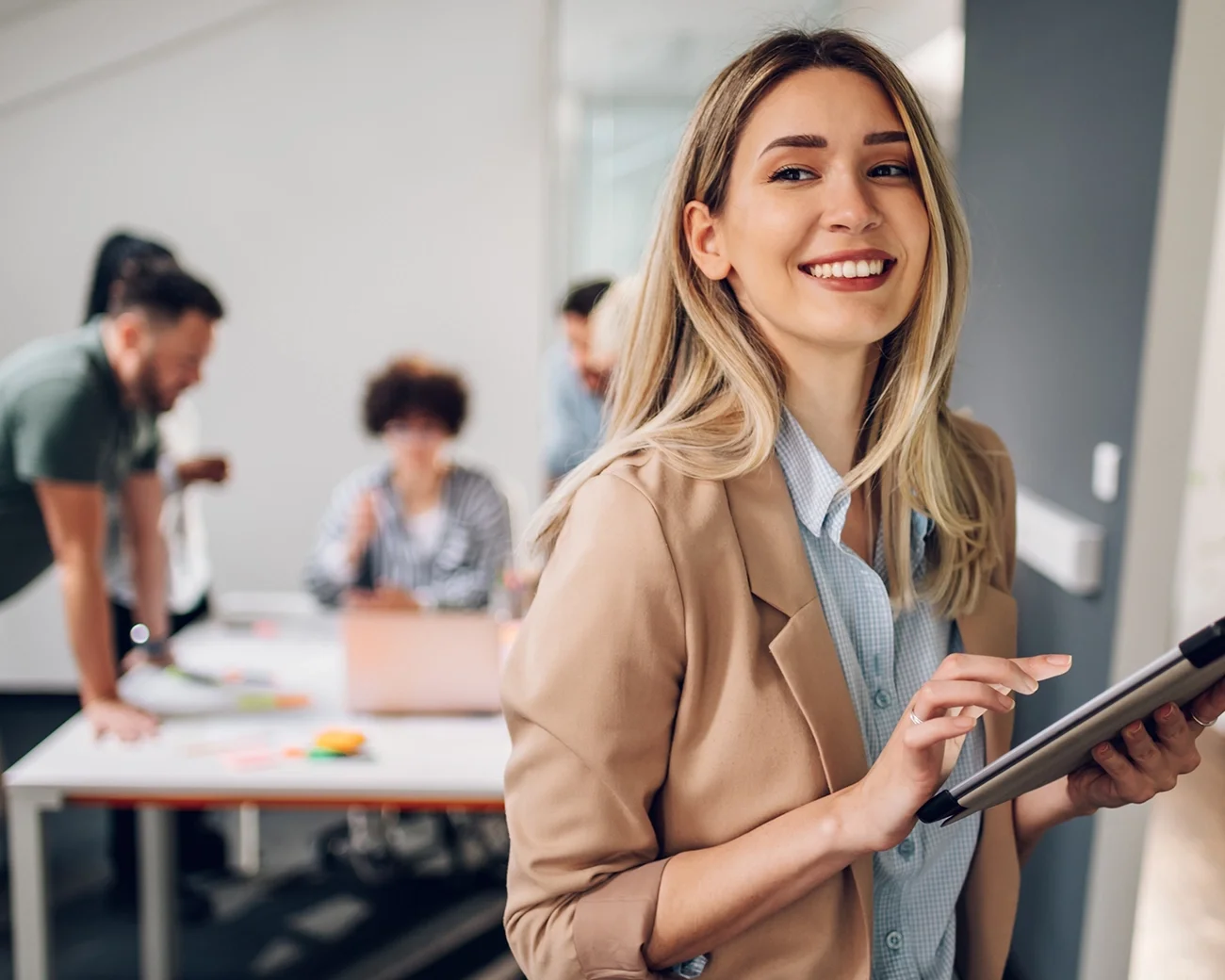 Zelfverzekerde vrouw met tablet in een werkruimte met collega's op de achtergrond