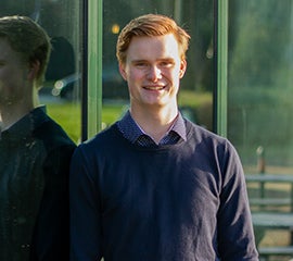 Jongen met rood haar en donkerblauw overhemd staat buiten met weerspiegeling in het raam