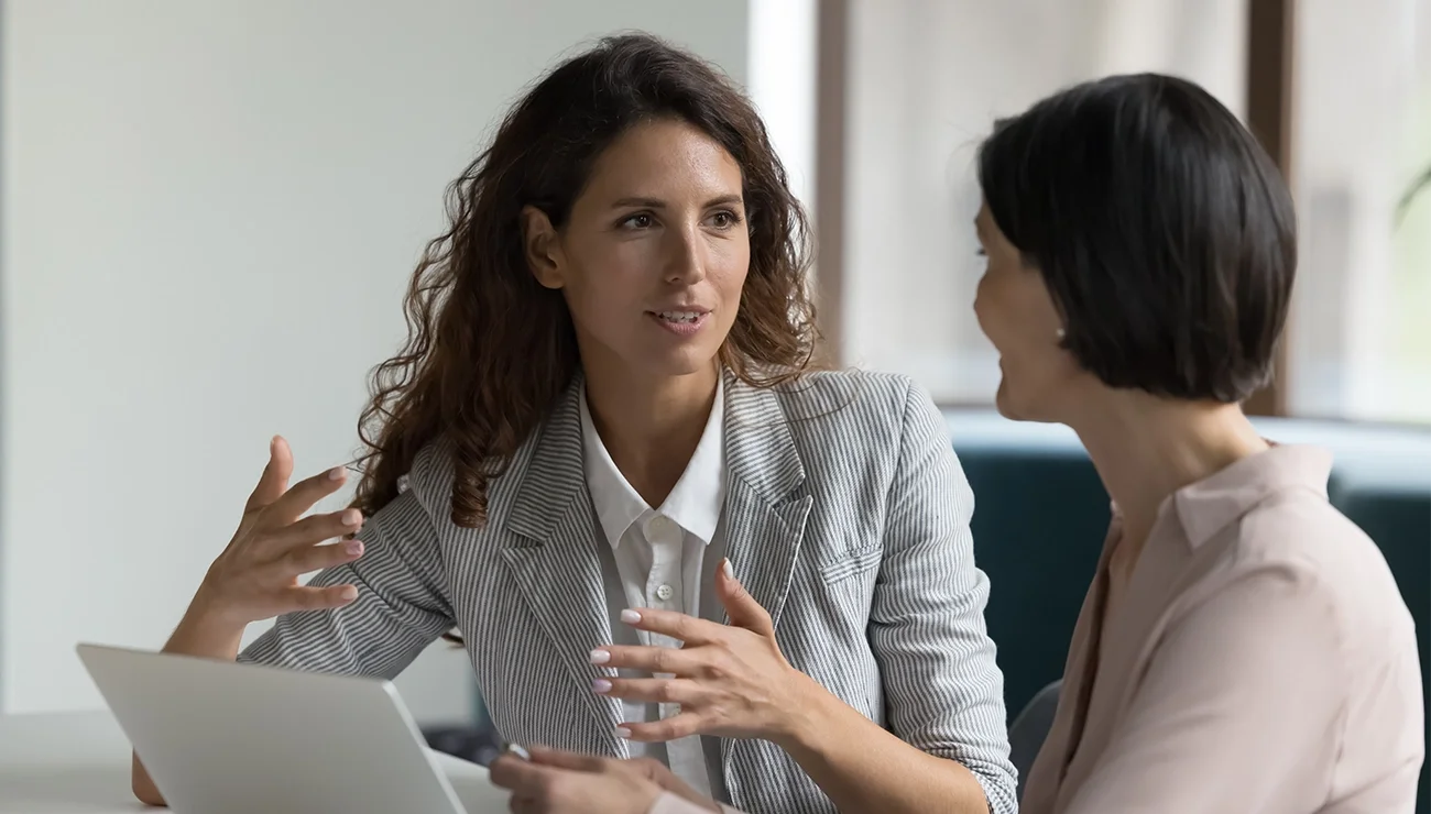 Twee mensen zitten tegenover elkaar aan een tafel en voeren een gesprek