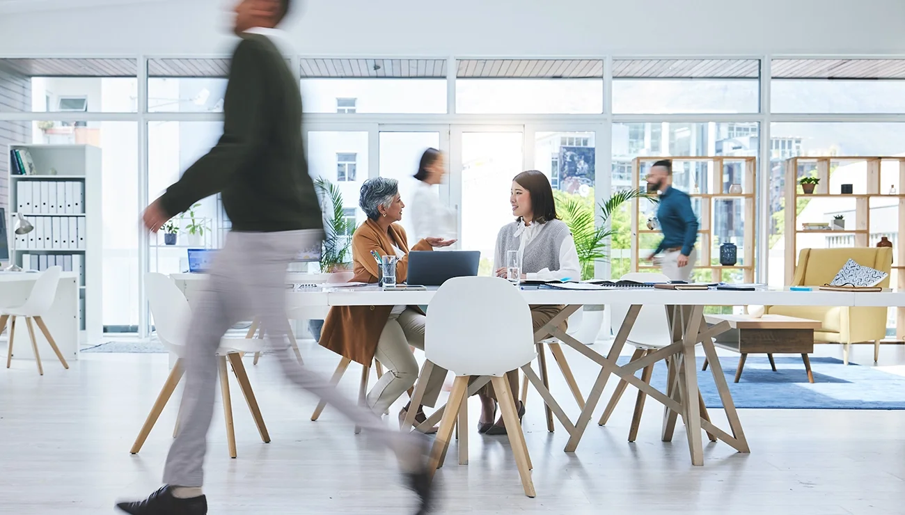 Collega's aan tafel in gesprek omringd door bewegende mensen