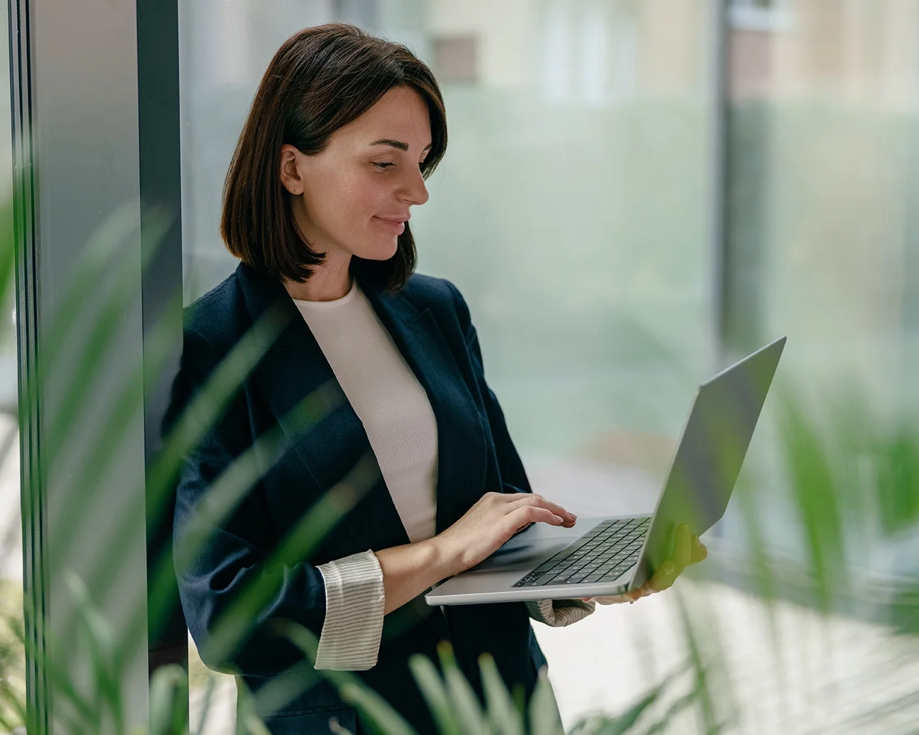 Vrouw leunt met laptop tegen raamkozijn