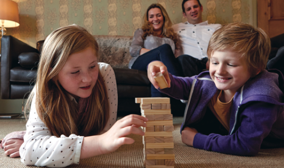 Image of a family with two children in the foreground playing a building-block game