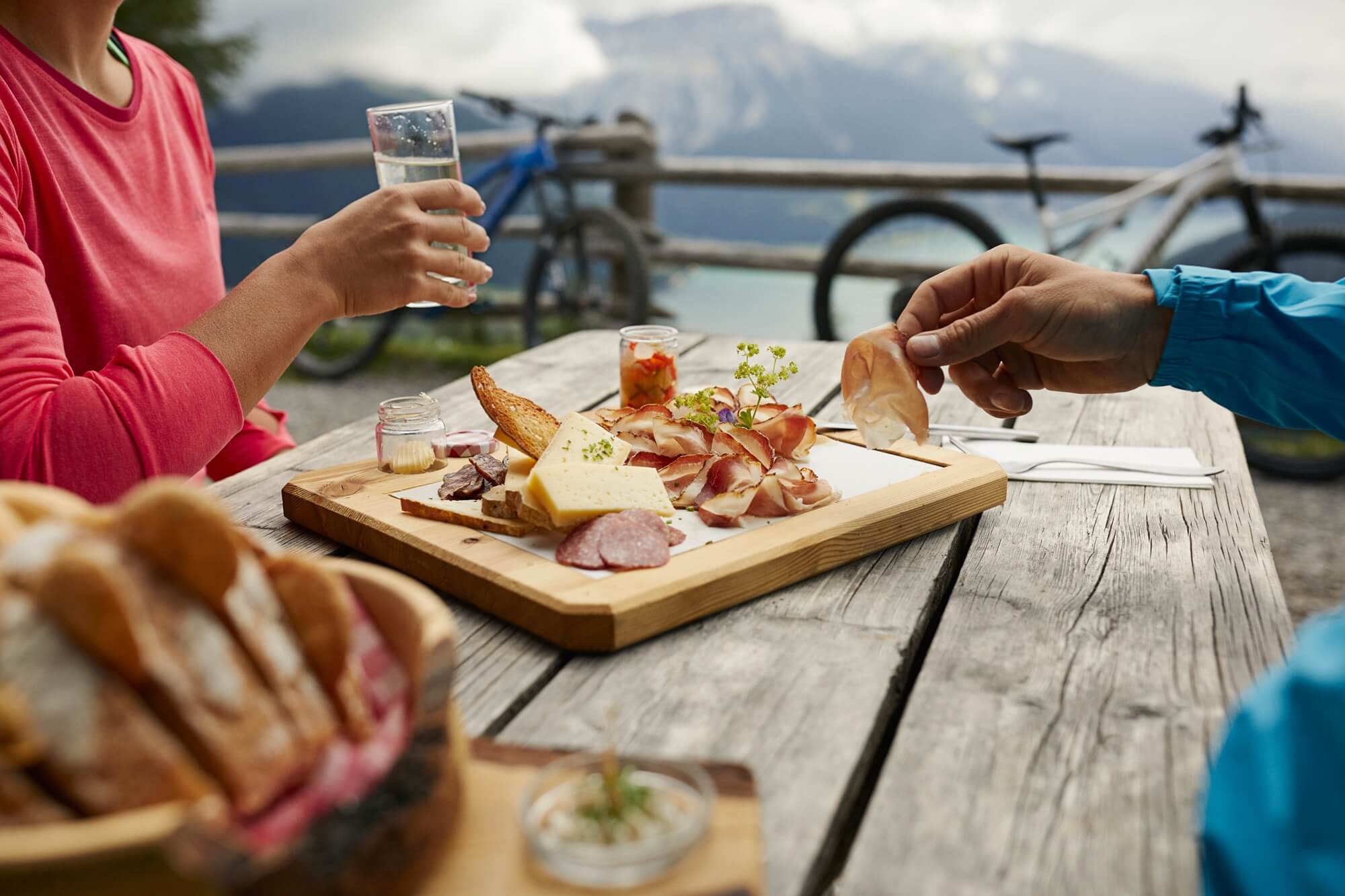 Zwei Personen machen eine Marende mit Südtiroler Speck g.g.A. am Tisch im Freien