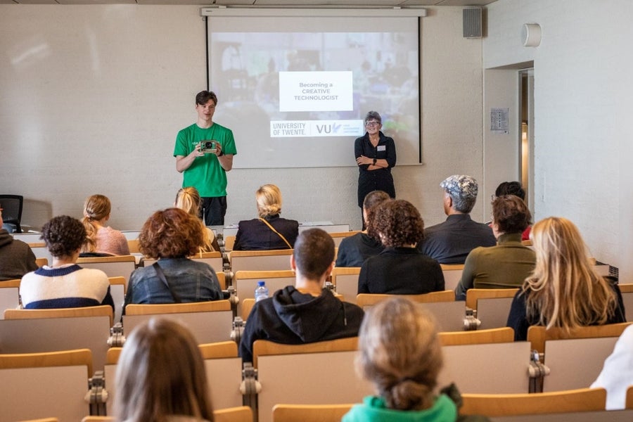 Two people standing in front of a large screen in lecture hall full of students