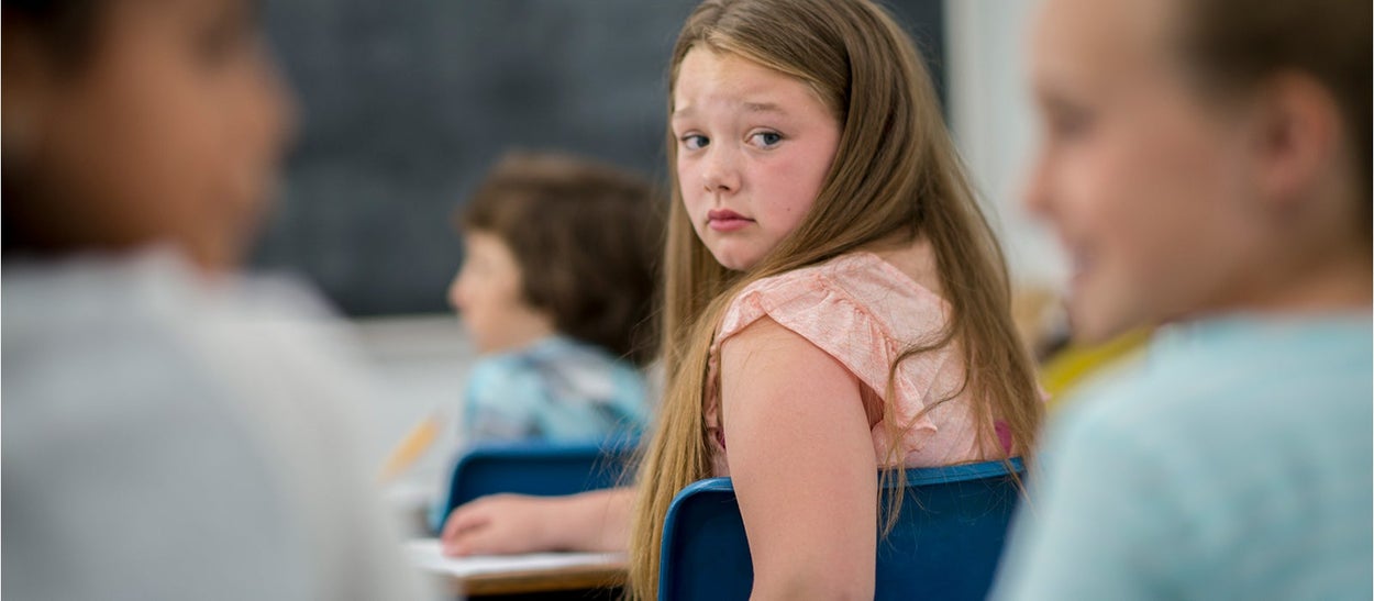 Girl in school class looks back at two children who talk to each other