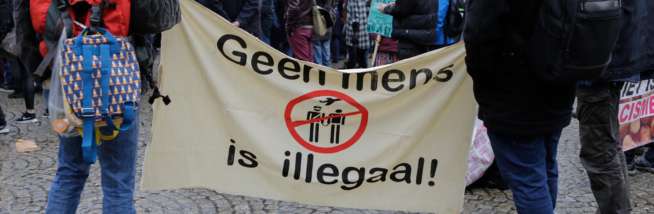 Two people hold a banner saying no human being is illegal