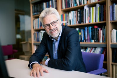 A man sitting behind a table with a bookshelf behind him