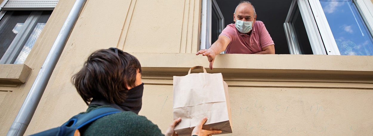 Een man neemt via het open raam een tasje met boodschappen aan van iemand 