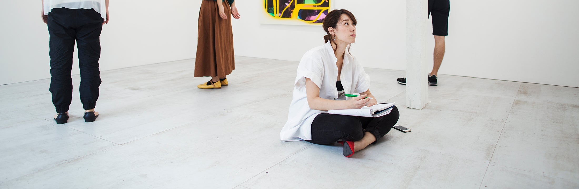 Vrouw zit op de grond voor een kunstwerk in een museum en maakt schetsen.