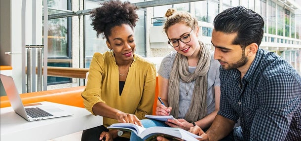 Three alumni sitting together and looking into a book