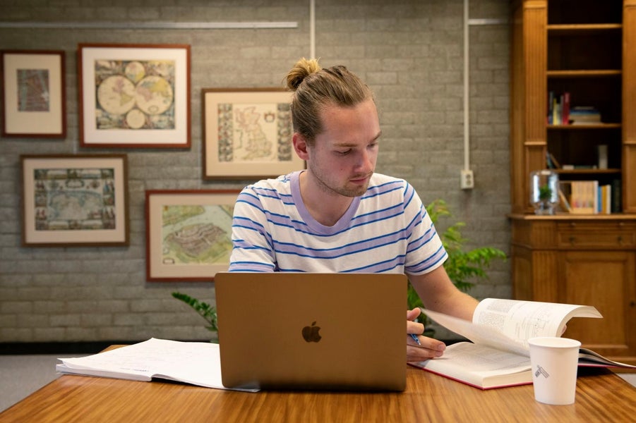 Een man aan een bureau met een laptop en een boek